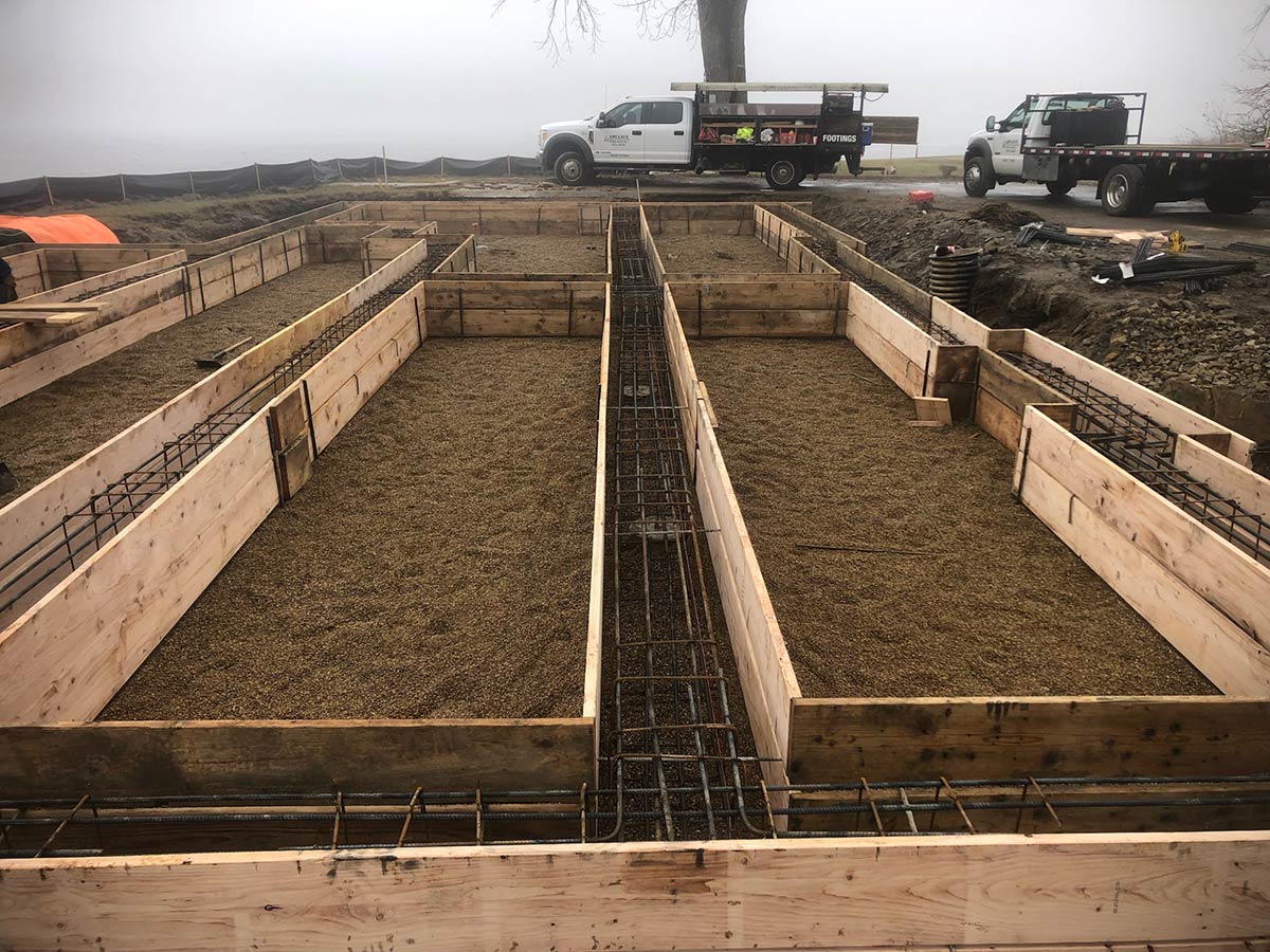 footings reinforced with rebar ready to be poured with concrete with trucks in the background